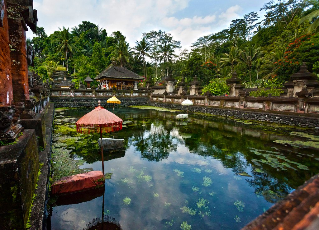 Templo Tirta Empul com arquitetura balinesa e uma grande piscina de água natural no centro com bordas de pedra.  Está ilustrando o post sobre o que fazer em Ubud.