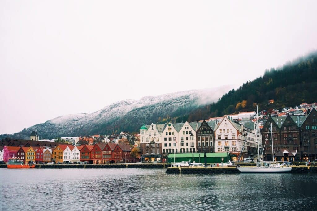 Edifícios de madeira coloridos margeiam a orla com montanhas nevadas ao fundo e um céu nublado em Bergen, que pode ser visitado com o eSIM Noruega.
