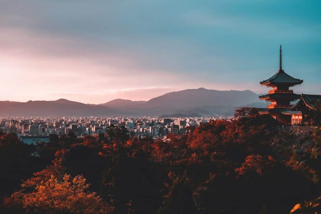 Vista de Kiyozumi Dera, em Kyoto, no Japão, com um templo de um lado em construção de pagode, com flores e vegetação e, do outro, a cidade moderna em contraste. Representa eSIM Japão.