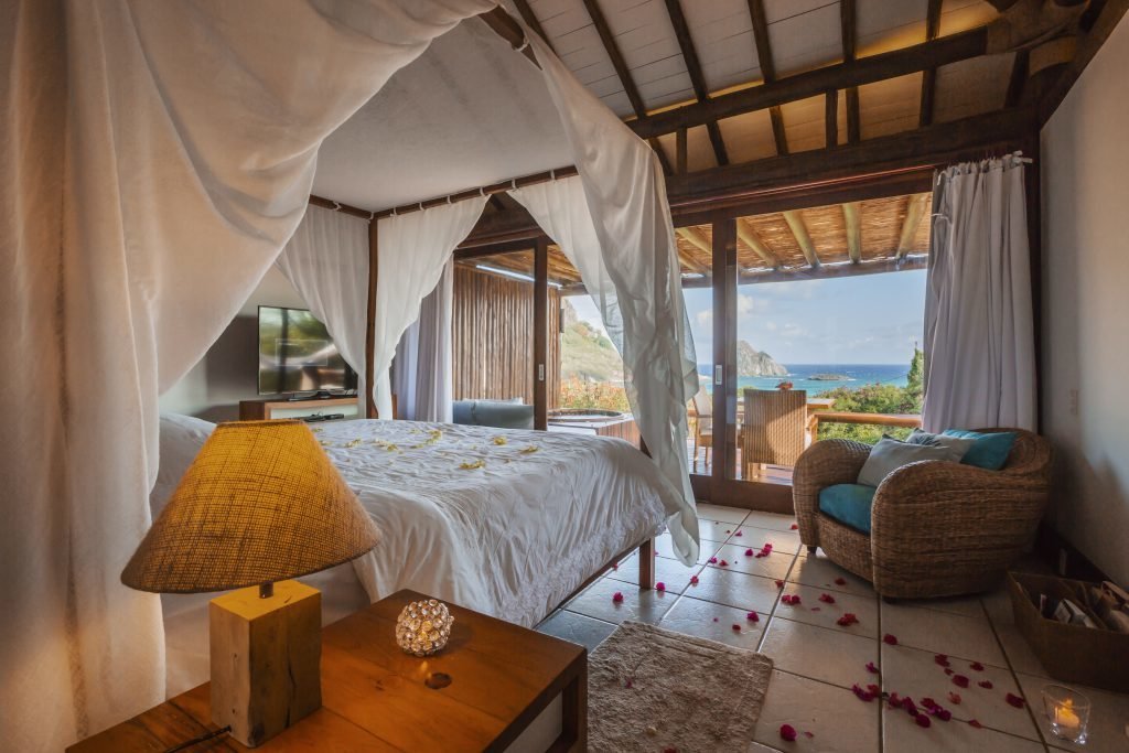 Bangalô com cama ampla, poltrona e pétalas de rosa na Pousada Maravilha