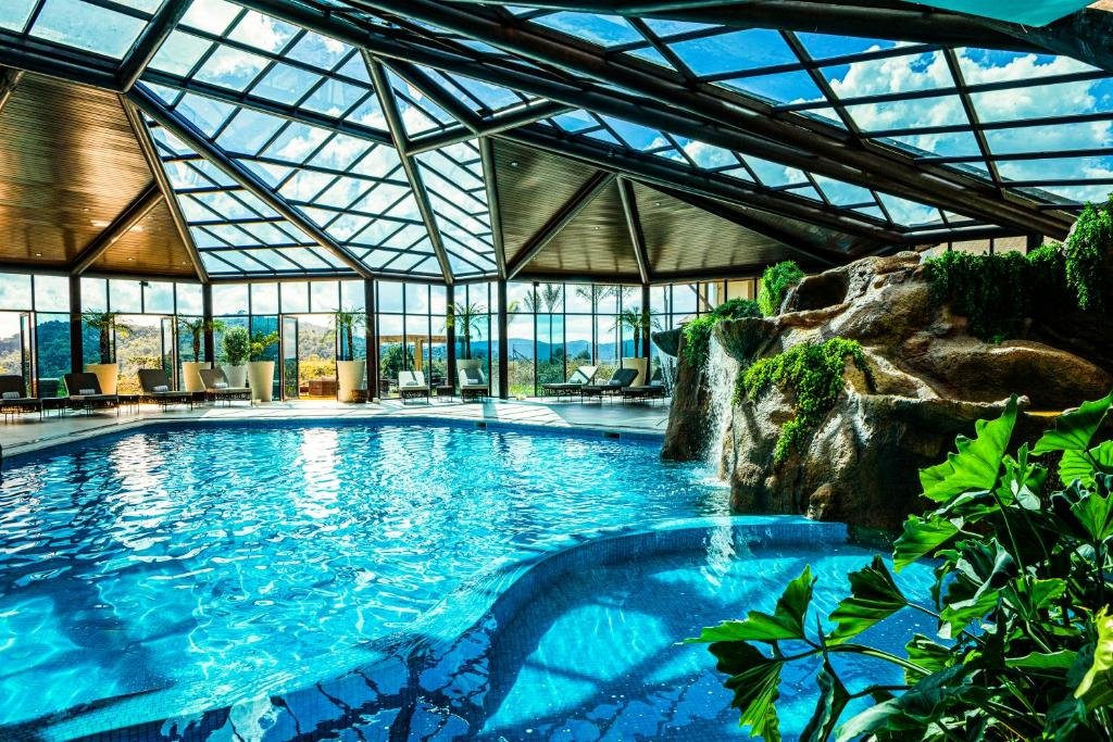 Piscina do Bendito Cacao Resort & Spa coberta com uma estrutura de vidro em que é possível ver a serra ao redor