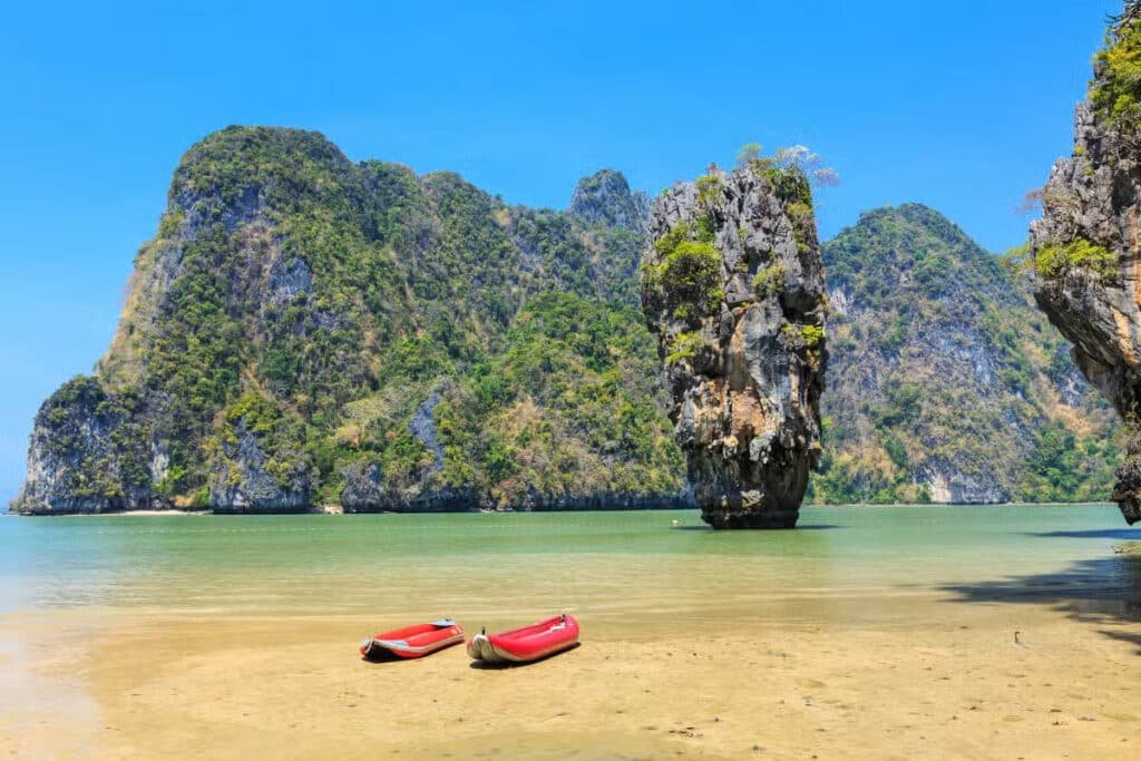 Uma vista panorâmica da ilha de James Bond com dois caiaques vermelhos, águas calmas e azul-turquesa e imponentes penhascos de calcário sob um céu azul claro.