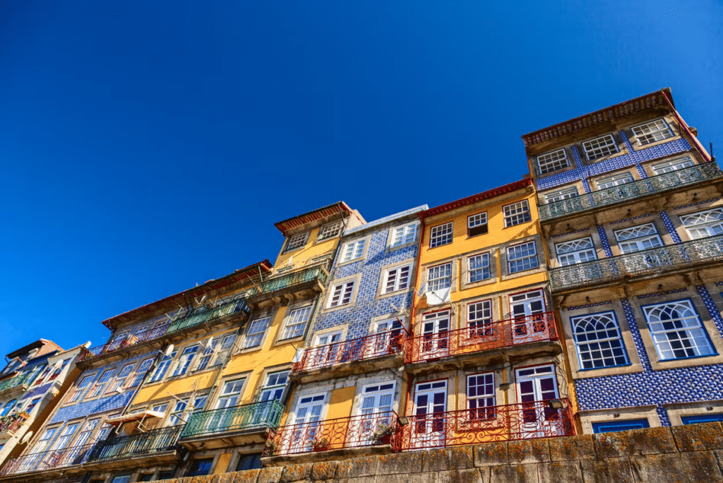 Fachada de prédios coloridos em estilo histórico com azulejos coloridos e sacadas em ferro trabalhadas na Ribeira, no Porto