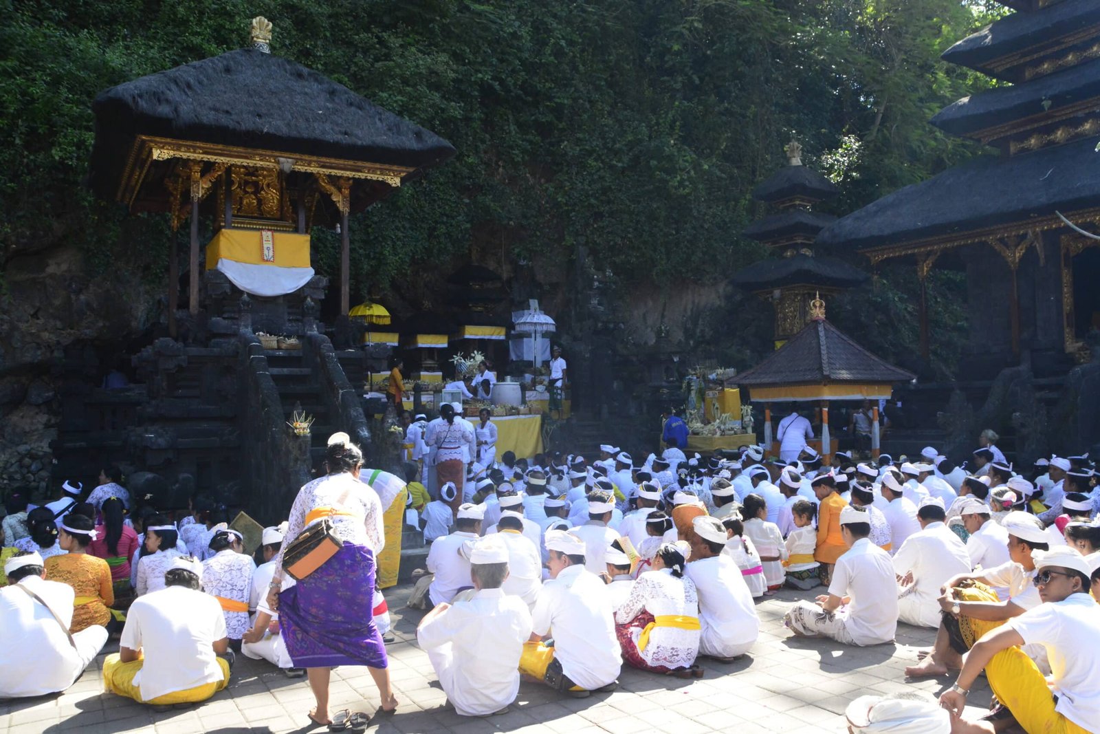 Várias pessoas com vestimentas tradicionais balinesas sentadas no chão em frente para o santurário no templo Pura Goa Lawah.  Está ilustrando o post sobre o que fazer em Ubud.