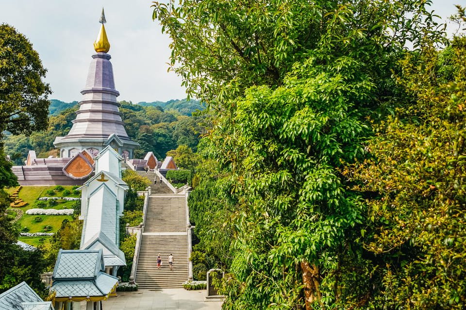 Um templo no Parque Nacional Doi Inthanon com uma torre dourada é cercado por árvores exuberantes, com uma escadaria que desce. Imagem para ilustrar post sobre o que fazer na Tailândia.