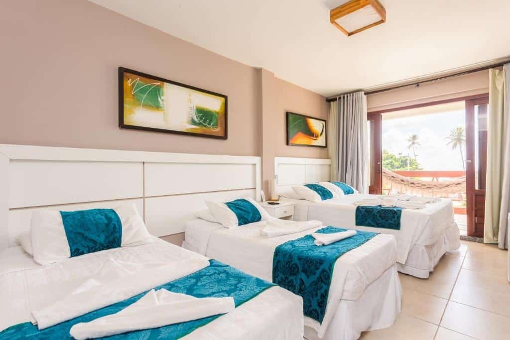 Quarto da Pousada Iandê. Duas camas de solteiro e uma cama de casal no lado esquerdo. No fundo a varanda do quarto com rede. Foto para ilustrar post sobre pousadas em Ipojuca.