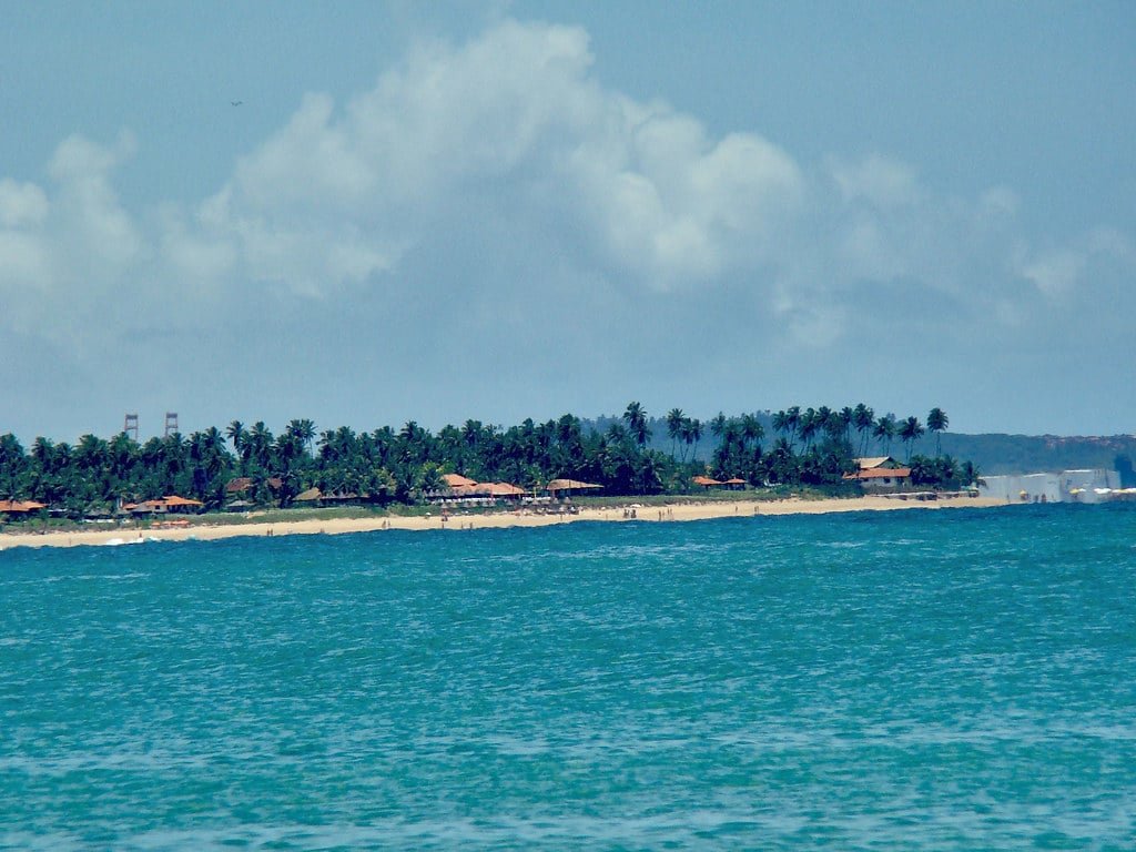 Vista do mar da Praia de Muro Alto em Ipojuca. Atrás do mar, no fundo, a vista da areia da praia com árvores.