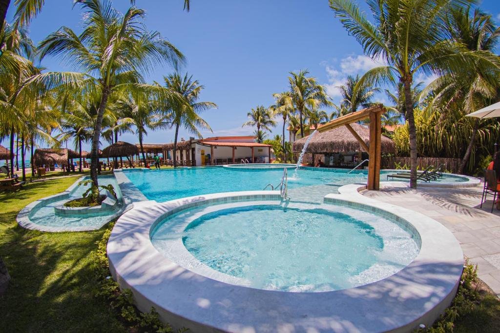 Piscina ao ar livre do Privê Pontal de Maracaipe. Uma piscina no meio, com uma cascata, ao redor árvores e no fundo a praia.