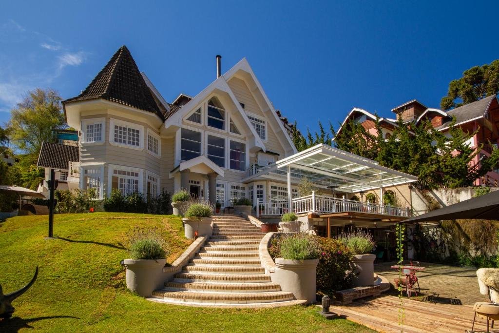 Propriedade do Secreto Boutique Hotel em uma construção ampla, com janelas amplas de vidro, uma escadaria de concreto com arbustos, e uma varanda coberta e um gramado ao redor