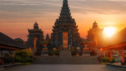 Um complexo de templos tradicionais balineses no templo Besakih ao pôr do sol, com uma torre central e duas estruturas menores, contra um céu colorido. Representa Bali.