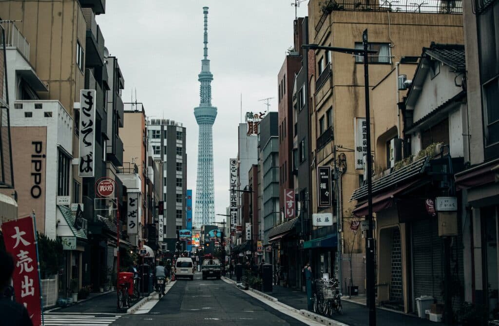 Bairro onde fica localizada a Tokyo Skytree, rua estreita com casas, comércios, carros e pedestres. Ao fundo um arranha-céu para representar o seguro viagem Tóquio. 